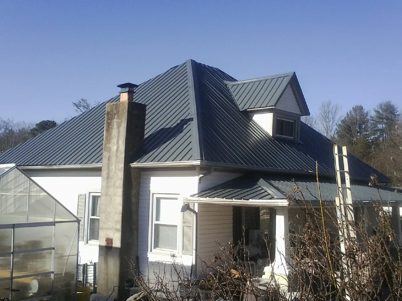 Dark blue standing seam metal roof on a white farmhouse with dormer — Slate & Tile Roof Repair by Roofing Brothers in Pillager
