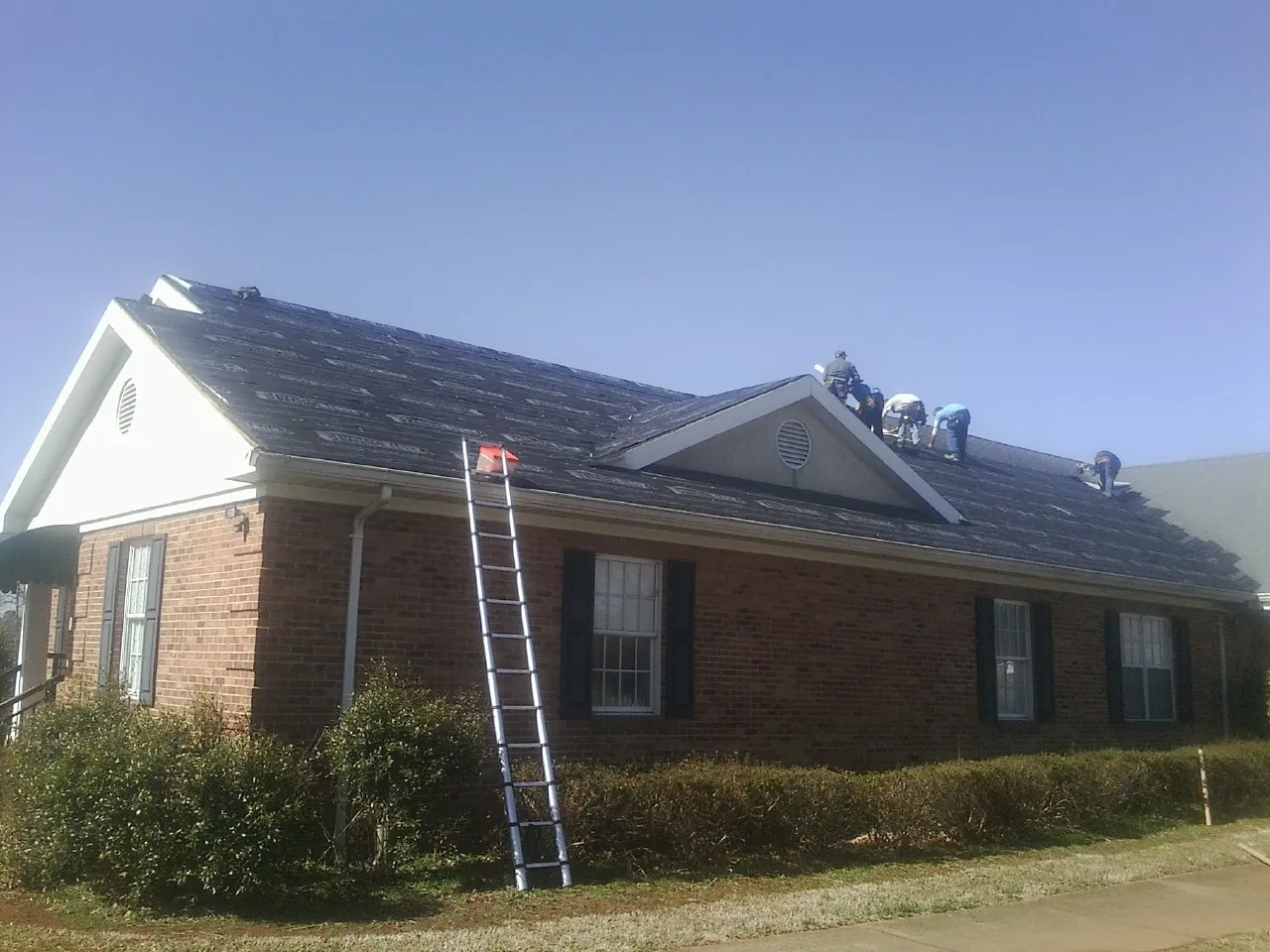 Crew tearing shingles off a brick ranch roof with a ladder set — Emergency Roof Repair work by our crew in Pillager