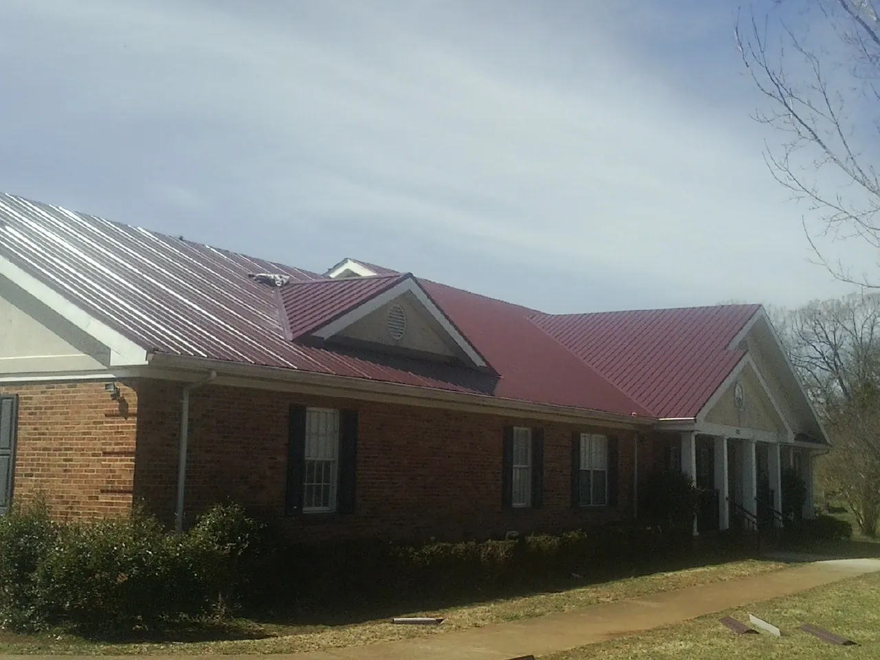 Red metal roof with gabled entries on a long brick building, from a Hail Damage Roof Repair job in Pillager