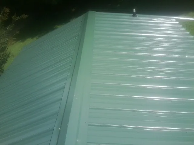 New green metal panels meeting at the ridge of a roof — Flat Roof Repair work by our crew in Pillager