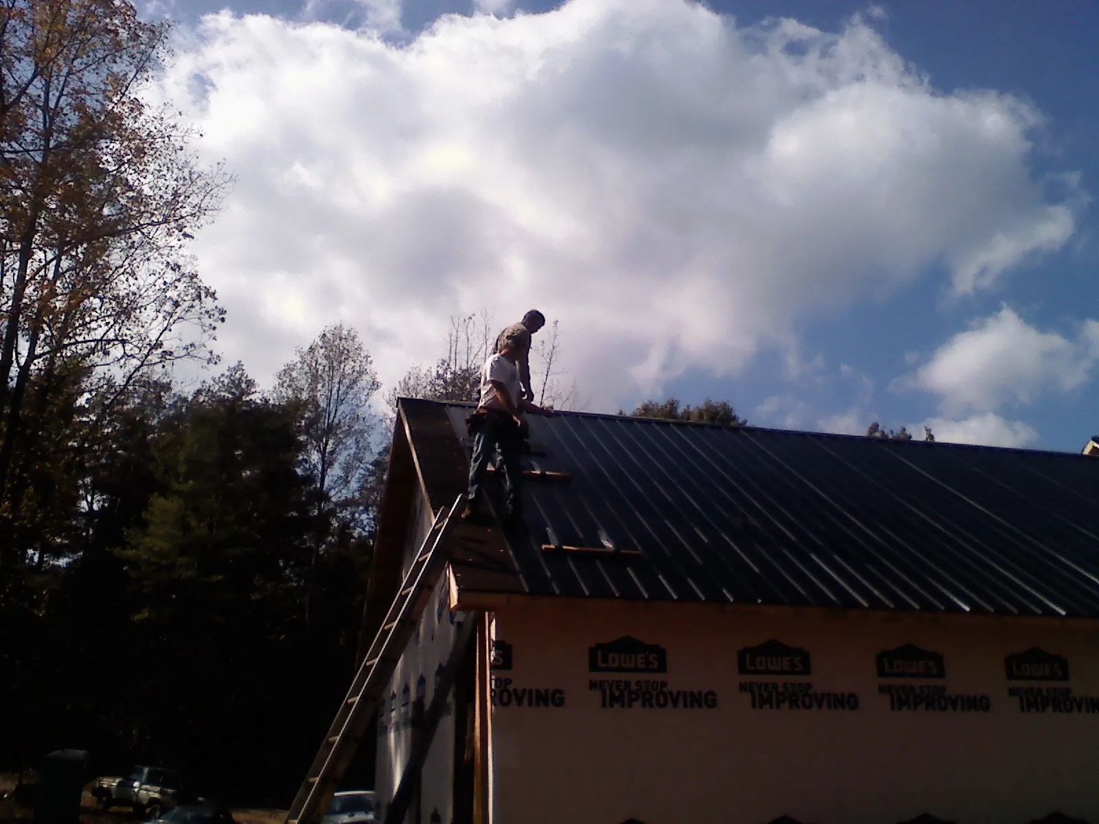 Roofer fastening dark metal panels high against a cloudy sky, from a Roof Inspection job in Pillager