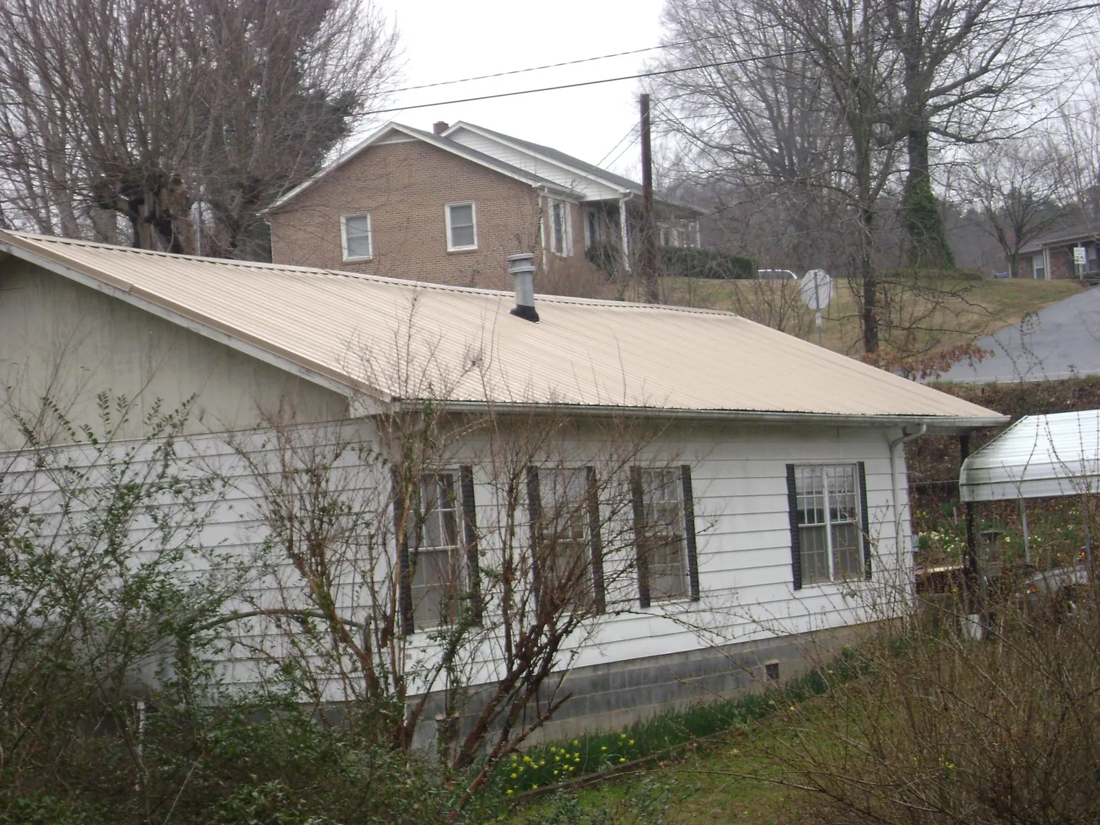 Tan metal roof on a white sided house set into a hillside — Commercial Roofing by Roofing Brothers in Pillager