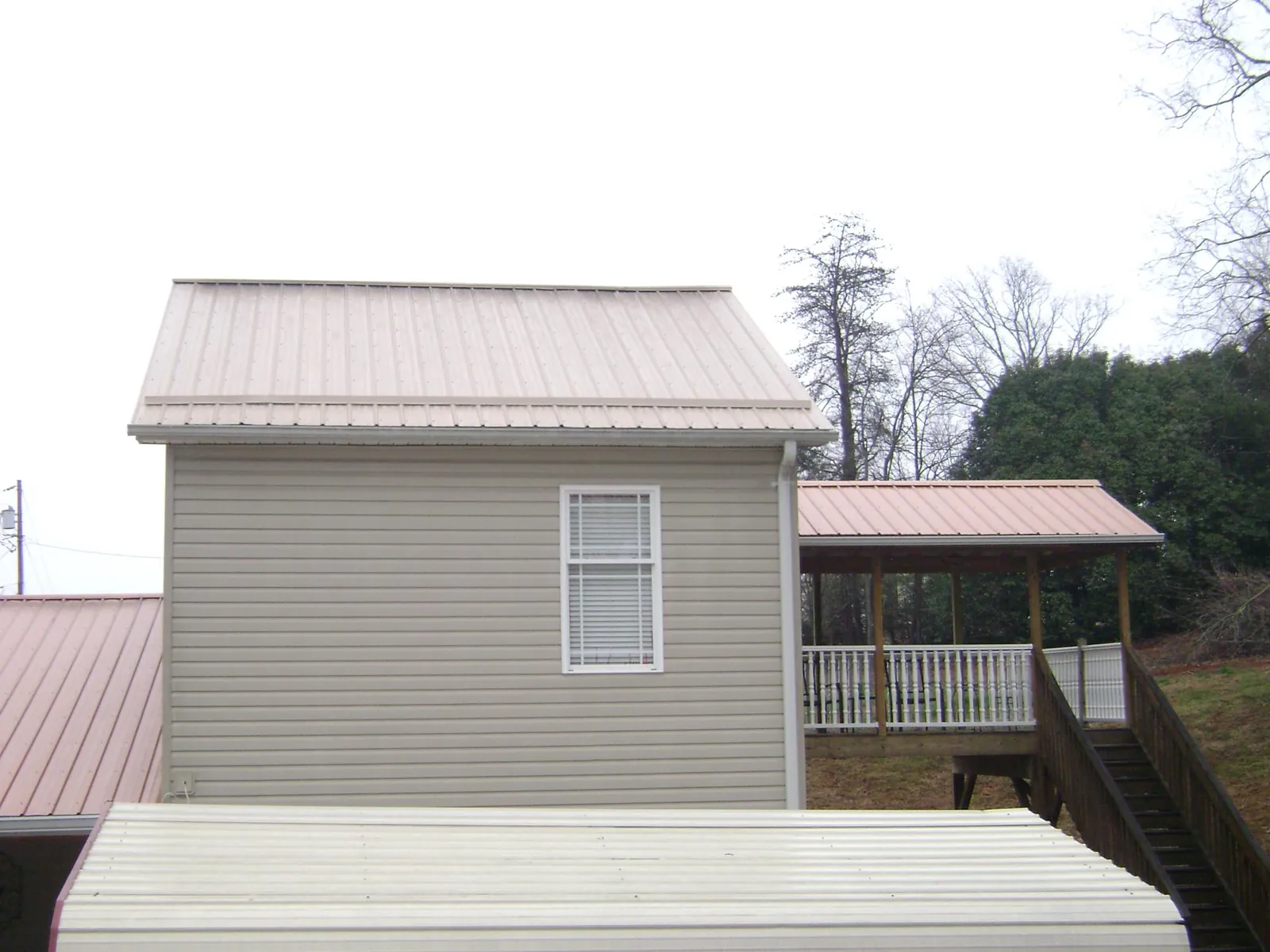 Tan metal roofs on a two story addition and attached porch, from a Roof Replacement job in Pillager